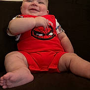 Carson is registered to the contest to win money with this photo: baby, child, smiling, red_clothing, spiderman, couch, indoor, happy, infant, person, cute, sitting, plush, skin, feet, arms, legs, head, portrait, relaxed