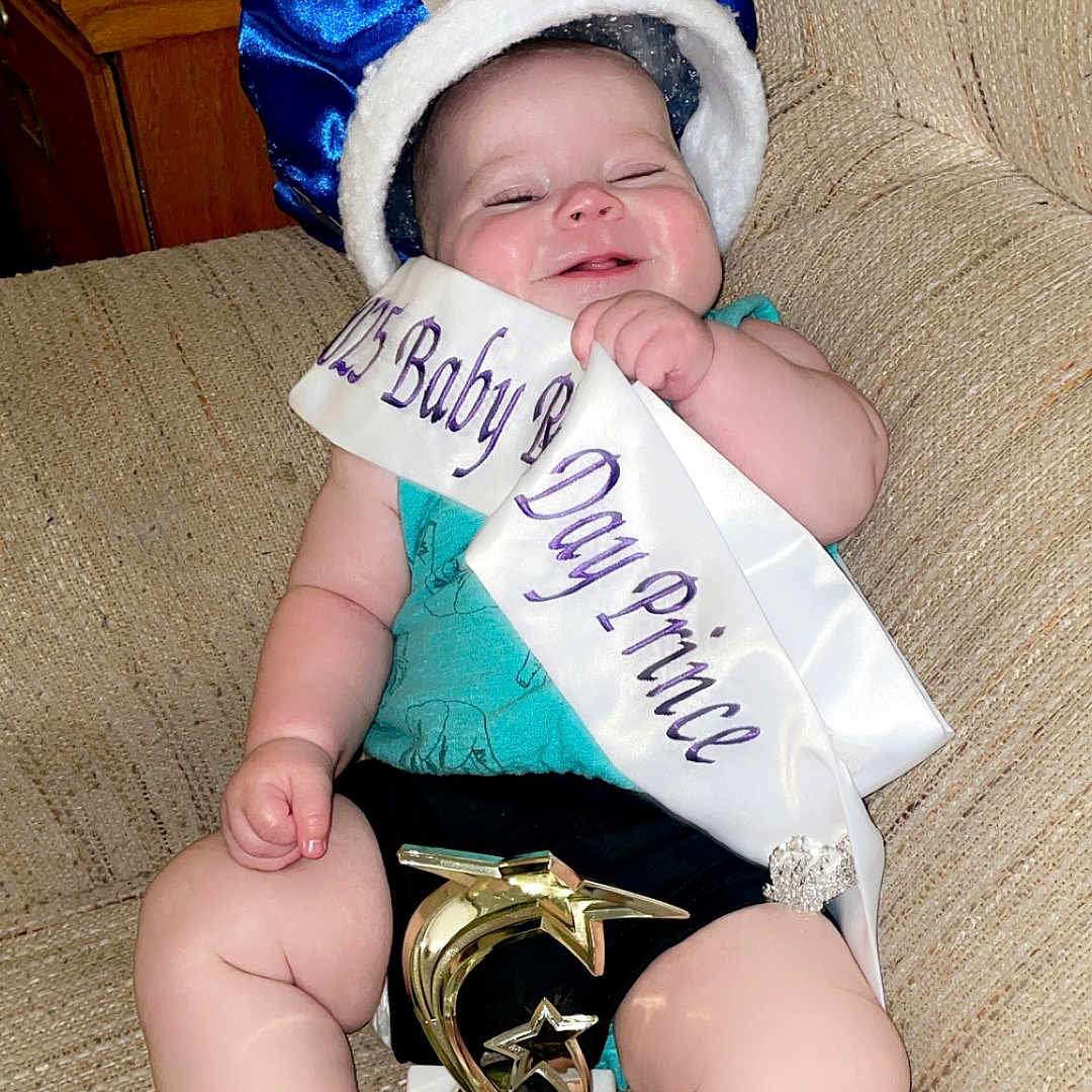 Carson joined the competition — help win amazing prizes! award, baby, celebration, child, clothing, couch, crown, cute, furniture, happy, headwear, indoor, person, portrait, sash, sitting, smiling, sock, sofa, trophy
