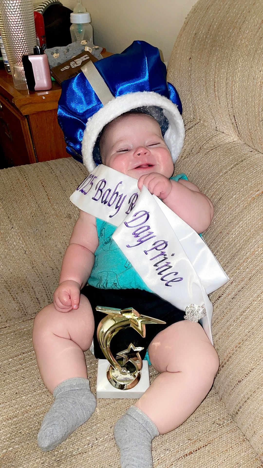 Carson joined the competition — help win amazing prizes! baby, crown, sash, trophy, sofa, couch, smiling, happy, indoor, child, clothing, sitting, award, celebration, sock, furniture, person, headwear, portrait, cute