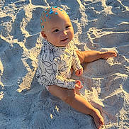 Alana joined the competition — help win amazing prizes! baby, child, sand, beach, sunlight, smile, face, head, gems, skin, barefoot, long_sleeve, floral_pattern, sitting, outdoor, nature, cute, playful, vacation, summer