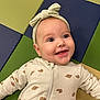 baby, smiling, headband, onesie, croissant_pattern, lying_down, colorful_mat, padded_mat, happy, infant, child, cute, face, eyes, mouth, clothing, indoors, baby_girl, head, skin