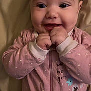Emery is registered to the contest to win money with this photo: baby, child, smiling, face, hands, onesie, pink_clothing, polka_dots, happy, infant, cute, portrait, eyes, mouth, fingers, sleeves, zipped, indoor, soft_light, expression