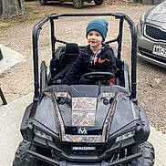 Zayden is registered to the contest to win money with this photo: child, toy_car, beanie, hoodie, outdoor, driveway, vehicle, smiling, parked, tree, car, wheel, tire, license_plate, gravel, concrete, person, casual_clothing, daylight, play