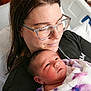 newborn, baby, adult, glasses, hospital_bed, blanket, portrait, closeup, face, skin, person, holding, caring, indoor, comfort, family, love, mother, child, rest
