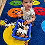 toddler, child, toy, animal_toy, plastic_toy, carpet, colorful, blue_bin, indoor, playroom, floor, furniture, cabinet, storage, clothing, white_shirt, shorts, face, expression, earring