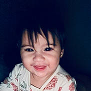 Dannha is registered to the contest to win money with this photo: baby, bangs, candid, child, closeup, dark_background, earring, eyes, face, floral_pajamas, hair, happy, indoor, mouth, person, portrait, skin, smile, teeth, toddler