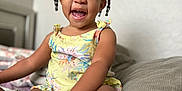 Amiyah is registered to the contest to win money with this photo: toddler, child, smiling, indoor, bed, braided_hair, beads, yellow_romper, happy, person, skin, face, hand, legs, furniture, pillow, home, cute, portrait, seated