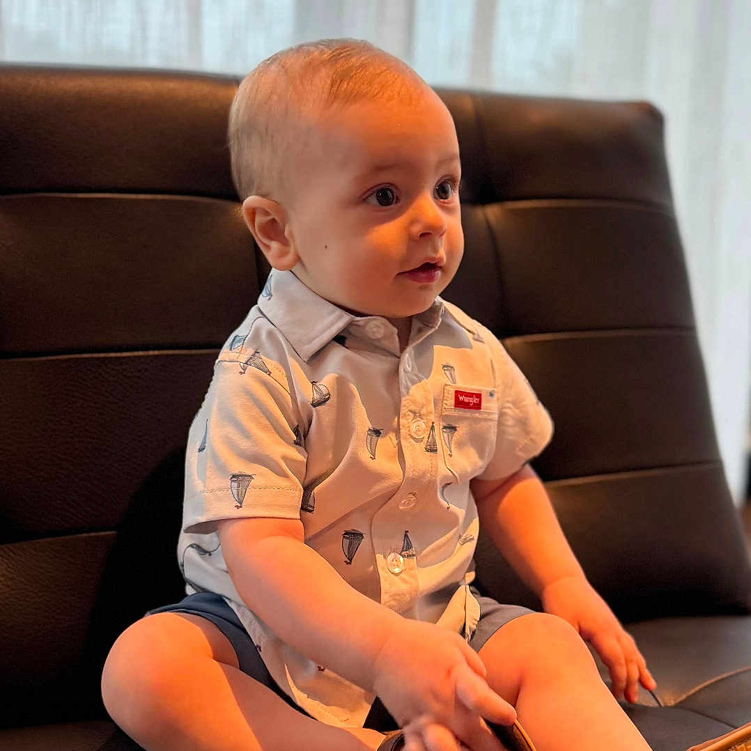 Timothy joined the competition — help win amazing prizes! toddler, child, sitting, indoor, leather_chair, shirt, footwear, curtain, light, portrait, baby, cute, casual_clothing, young_child, sole, hand, face, head, expression, comfort