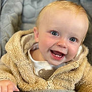 Bailey is registered to the contest to win money with this photo: baby, smiling, child, fuzzy_jacket, stroller, handle, blue_eyes, teeth, closeup, happy, infant, cute, warm_clothing, hand, face, portrait, indoor, cozy, expression, person