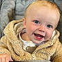 baby, smiling, child, fuzzy_jacket, stroller, handle, blue_eyes, teeth, closeup, happy, infant, cute, warm_clothing, hand, face, portrait, indoor, cozy, expression, person