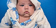 Layla is registered to the contest to win money with this photo: baby, child, infant, hooded_robe, fluffy_clothing, blue_background, cute, chubby_cheeks, portrait, sitting, serious_expression, soft_texture, warm_clothing, indoor, person, young_child, closeup, skin, face, head