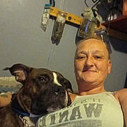 Tigger is registered to the contest to win money with this photo: animal, brown_dog, casual, chain_collar, closeup, companion, dog, face, furniture, indoor, person, pet, portrait, relaxed, shelf, smiling, tank_top, tools, wall, woman