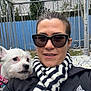 Asha is registered to the contest to win money with this photo: woman, dog, white_dog, sunglasses, striped_scarf, selfie, outdoor, blue_fence, patio_tiles, jacket, adidas_logo, small_dog, pet, portrait, smiling, human_face, animal_face, railing, trees, pink_collar