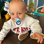 Petru participe au concours pour gagner de l'argent avec cette photo : baby, pacifier, crawling, white_sweater, red_letters, wooden_floor, toys, play_area, indoor, child, smiling, happy, person, flooring, cute, young_child, playtime, home, colorful, infant