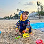 Rebecca joined the competition — help win amazing prizes! toddler, child, beach, sand, shovel, toy, hat, sunset, outdoor, play, colorful_clothing, barefoot, smiling, sitting, nature, palm_trees, vacation, summer, happy, sand_toys