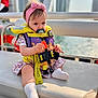 Rebecca joined the competition — help win amazing prizes! baby, child, life_jacket, pink_headband, pacifier, floral_dress, white_socks, toy, boat, water, city_skyline, sunlight, outdoor, sitting, bench, safety, cute, serious, portrait, daytime