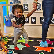 Zariyah is registered to the contest to win money with this photo: toddler, child, adult_hand, colorful_carpet, stars, indoor, playroom, toys, smiling, walking, baby, clothing, jeans, socks, learning, education, play, person, holding_hand, cute