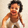 toddler, child, baby, curly_hair, smiling, laughing, portrait, indoor, carpet, kneeling, sitting, brown_shirt, white_pants, short_sleeves, outstretched_hand, happy, face, person, warm_lighting, home