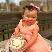 Grace joined the competition — help win amazing prizes! toddler, child, smile, dress, pink, bow, cake, plastic_cover, bench, outdoor, park, curly_hair, happy, sitting, cute, food, celebration, portrait, person, daylight
