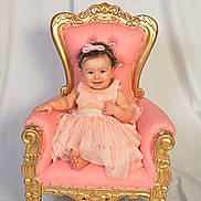 Grace is registered to the contest to win money with this photo: baby, child, girl, dress, headband, smile, chair, throne, pink, gold, portrait, cute, indoor, happy, toddler, fabric, background, sitting, people, clothing