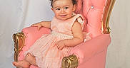 Grace is registered to the contest to win money with this photo: baby, chair, child, cute, dress, gold_detail, happy, headband, indoor, infant, ornate_chair, person, pink_chair, pink_dress, portrait, sitting, smile, studio, white_background, young_child