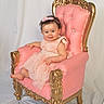 Grace is registered to the contest to win money with this photo: baby, child, pink_dress, headband, smile, chair, ornate_chair, gold_detail, pink_chair, portrait, studio, white_background, cute, sitting, infant, dress, happy, person, young_child, indoor