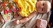 Anora is registered to the contest to win money with this photo: baby, infant, child, blanket, plush_blocks, yellow_top, floral_shorts, face, hand, milestone, soft_toy, indoor, cute, portrait, laying_down, colorful_clothing, smiling, skin, newborn, resting