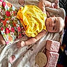 baby, blanket, child, colorful_clothing, cute, face, floral_shorts, hand, indoor, infant, laying_down, milestone, newborn, plush_blocks, portrait, resting, skin, smiling, soft_toy, yellow_top