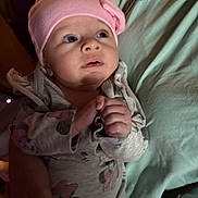 Anora is registered to the contest to win money with this photo: baby, infant, pink_hat, bow, clothing, onesie, mickey_mouse, hand, face, person, portrait, cute, child, indoor, holding, soft_lighting, expression, newborn, looking_up, warm