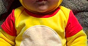 Anora is registered to the contest to win money with this photo: baby, child, costume, yellow, bear, hood, ears, blanket, cute, infant, clothing, red_sleeves, face, portrait, person, indoors, soft_texture, lying_down, expression, warm