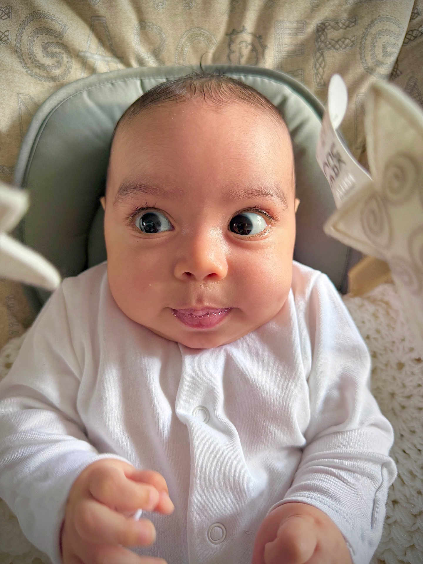 John joined the competition — help win amazing prizes! baby, infant, white_clothing, wide_eyes, cute, portrait, indoor, seat, cushion, soft_lighting, hands, face, expression, newborn, child, cozy, warm, skin, head, person