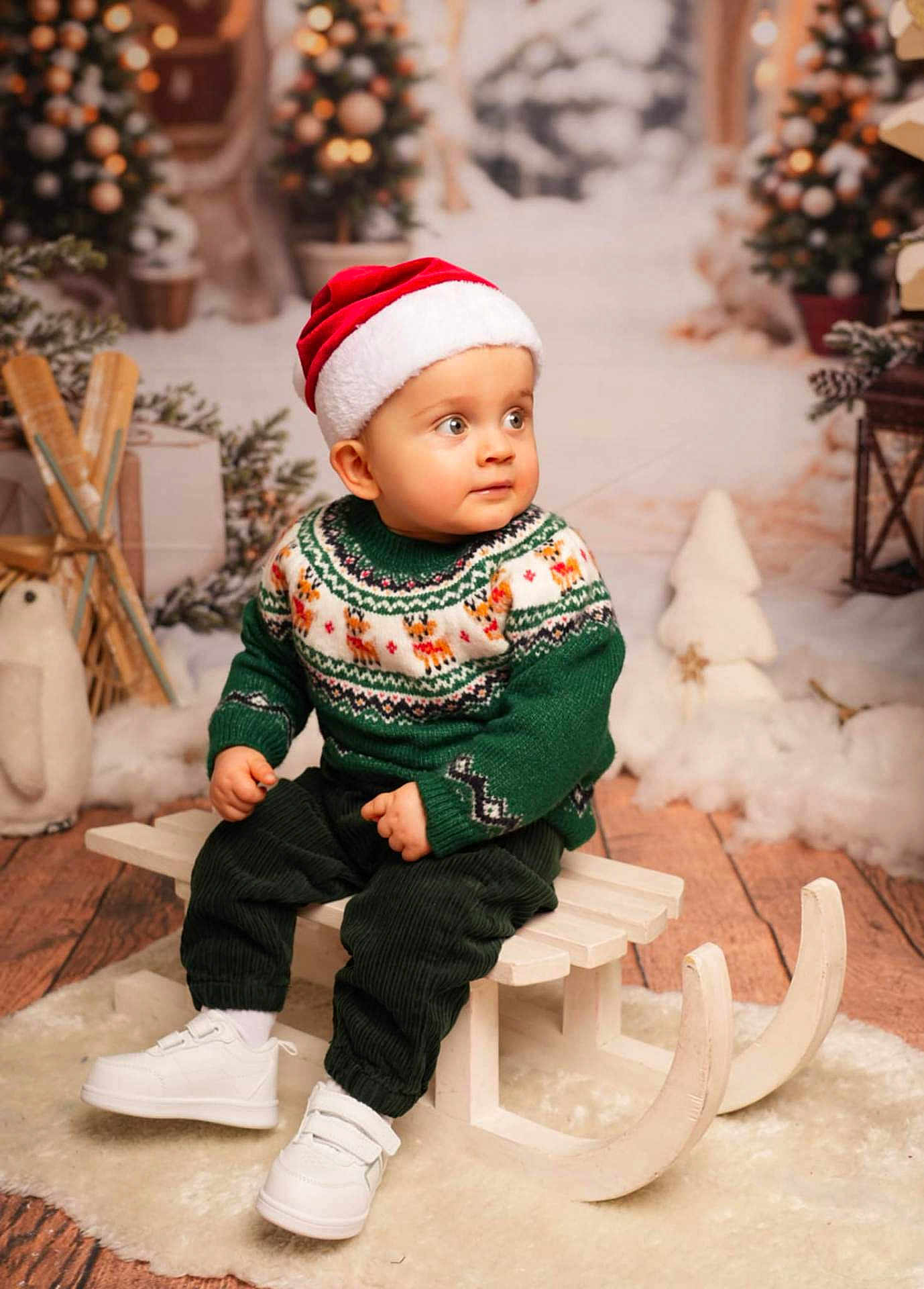 Mathis a rejoint le concours — aidez-le/la à gagner de superbes lots ! toddler, child, santa_hat, christmas_sweater, sled, winter, holiday, decorations, plush_toy, snow, festive, indoors, cute, smiling, white_shoes, wooden_floor, christmas_tree, cozy, portrait, seasonal