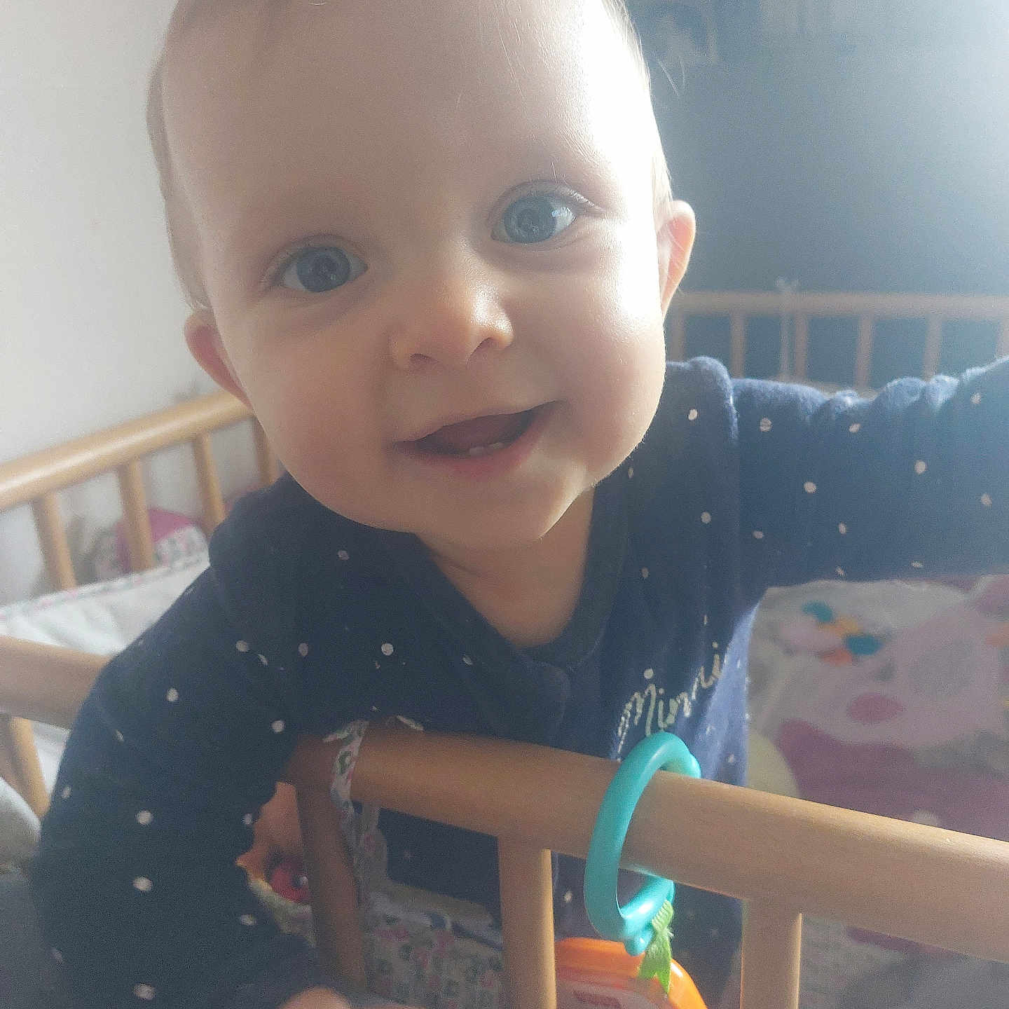 Willow participe au concours pour gagner de l'argent avec cette photo : baby, infant, crib, wooden_rail, polka_dot_clothing, smiling, happy, face, hand, nursery, soft_light, indoor, curious, person, child, cute, toy, blue_clothing, closeup, home