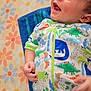 baby, infant, smiling, dinosaur_print, onesie, hand, face, happy, lying_down, blanket, floral_pattern, child, cute, skin, head, blue, green, orange, white, toddler