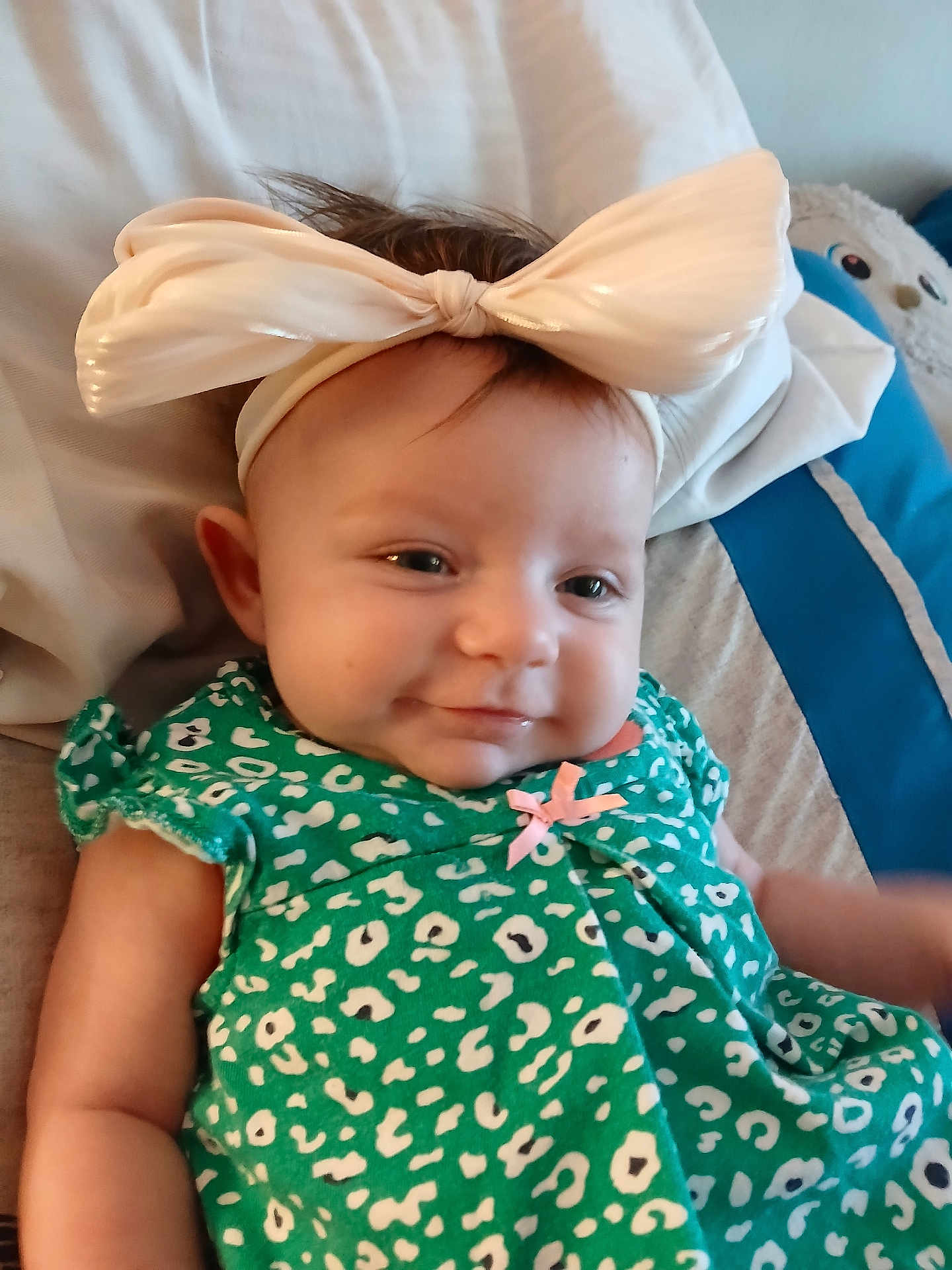 Brenleigh joined the competition — help win amazing prizes! baby, child, headband, bow, green_dress, patterned_clothing, smile, face, infant, cushion, bed, soft_lighting, happy, portrait, indoors, cute, young_child, resting, person, cozy