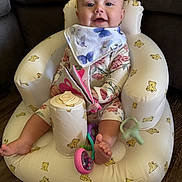 Patsy joined the competition — help win amazing prizes! baby, infant, child, inflatable_chair, teddy_bear_pattern, bib, floral_outfit, toy, soft_book, pink_toy, purple_toy, smiling, indoor, wood_floor, cute, seated, barefoot, happy, person, portrait
