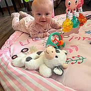 Patsy is registered to the contest to win money with this photo: baby, infant, play_mat, pink, toy, plush_toy, cow, rattle, floor, wooden_floor, furniture, smiling, cute, child, indoors, crawling, colorful, playtime, person, happy