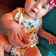 Patsy joined the competition — help win amazing prizes! adult_hand, baby, blue_eyes, child, comfort, couch, curious_expression, floral_pattern, hand, headband, indoor, infant, lap, onesie, person, pink, sitting, skin, white, yellow