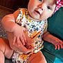 Patsy joined the competition — help win amazing prizes! adult_hand, baby, blue_eyes, child, comfort, couch, curious_expression, floral_pattern, hand, headband, indoor, infant, lap, onesie, person, pink, sitting, skin, white, yellow