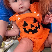 Patsy joined the competition — help win amazing prizes! baby, child, pumpkin_outfit, orange_clothing, headband, bow, face, person, indoor, tattoo, arm, skin, table, furniture, hair, blue_shirt, cute, holiday, festive, expression