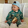 baby, child, infant, sitting, portrait, indoors, couch, blanket, quilt, baseball_cap, camouflage, sweatshirt, sneakers, milestone_sign, seven_months, wooden_sign, blue_eyes, serious_expression, furniture, family_photo