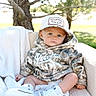 baby, child, infant, portrait, outdoor, sitting, blanket, chair, camouflage, hat, cap, clothing, shoes, white_shoes, grass, tree, nature, sunlight, serious_expression, close_up
