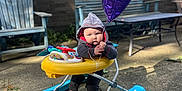 Ventus is registered to the contest to win money with this photo: baby, balloon, hoodie, walker, outdoor, patio, child, toy, purple_balloon, concrete, bench, chair, sunlight, brick_wall, greenery, person, clothing, footwear, play, daytime
