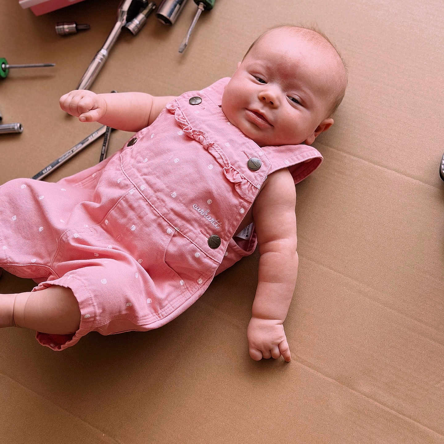 Karsyn is registered to the contest to win money with this photo: arm, baby, cardboard, child, cute, expression, face, furniture, hand, hardware, indoor, infant, lying_down, pink_romper, portrait, ratchet, screwdriver, toolbox, tools, worktools