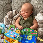 Karsyn joined the competition — help win amazing prizes! baby, infant, couch, blanket, toy, soft_toy, book, colorful, patterned, child, foot, arm, face, smile, indoor, fabric, play, education, cute, relaxed