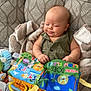 baby, infant, couch, blanket, toy, soft_toy, book, colorful, patterned, child, foot, arm, face, smile, indoor, fabric, play, education, cute, relaxed