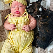 Karsyn joined the competition — help win amazing prizes! baby, child, dog, yellow_outfit, headband, blanket, lying_down, cute, pet, snuggling, indoor, infant, animal, friendship, cozy, patterned, soft_texture, skin, face, hand
