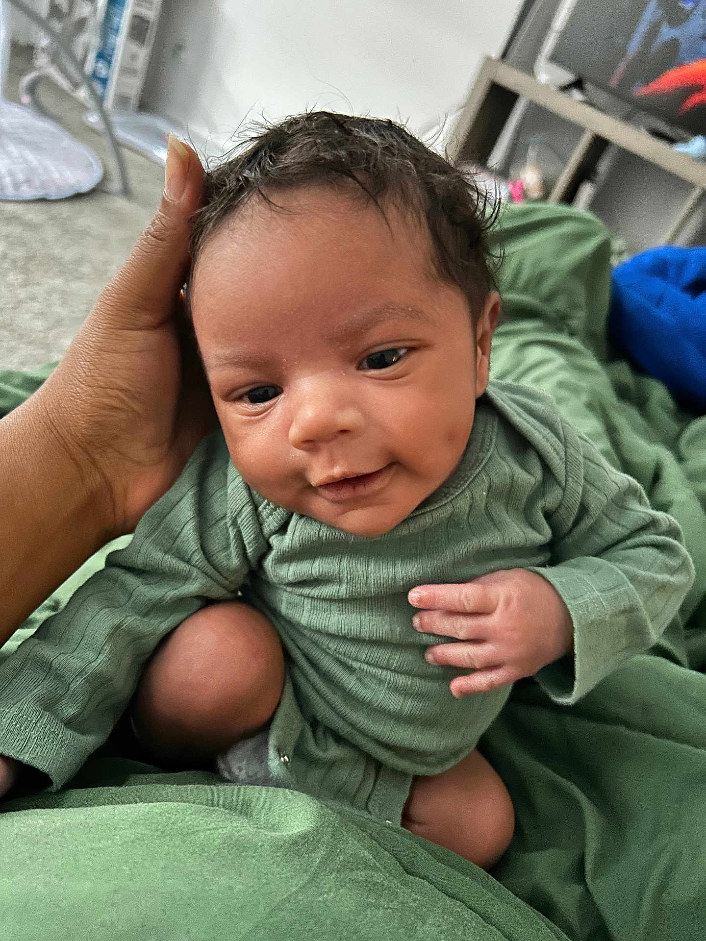 Tyus is registered to the contest to win money with this photo: baby, infant, hand, green_clothing, smile, face, skin, person, closeup, indoor, portrait, cute, child, newborn, resting, family, cozy, warm, soft_fabric, human