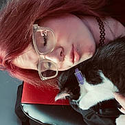 Nova is registered to the contest to win money with this photo: affection, animal, black_and_white_cat, black_chair, casual, cat, chair, close_up, comfort, cozy, cuddle, glasses, human_face, indoor, person, pet, portrait, purple_collar, red_chair, red_hair