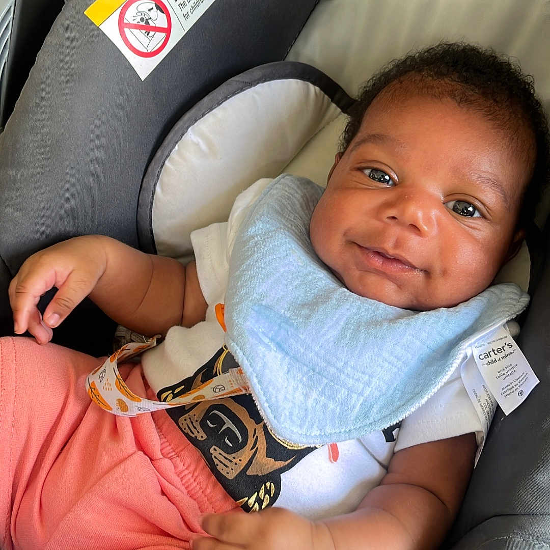 Kentrell joined the competition — help win amazing prizes! baby, infant, car_seat, smiling, bib, clothing, peach_shorts, happy, face, child, person, cute, baby_toddler, indoor, seat, warning_label, safety, relaxing, portrait, young_child